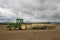 A farmer carries empty wooden bins for potatoes on a trailer towed behind a John Deere tractor across a farm field