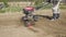 Farmer cultivates the soil in the garden using a tiller - motor cultivator. Man in hat and rubber boots. Footage 4k. Side view slo