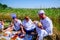 Farmer cuts bread with knife. People have breakfast on picnic