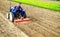 Farmer drives a tractor with a milling machine. Loosens, grind and mix soil on plantation field. Field preparation for new crop