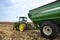 Farmer driving tractor and grain cart in farm corn field