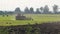 Farmer on farmland in modern red tractor with tillage unit, lots of small birds, white storks and cars in the foreground