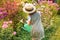 Farmer girl in summer straw hat. Little gardener farming, watering flowerbed with pink flowers, having fun in garden. Big green