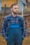 Farmer handsome european appearance male rural portrait with beard, shirt and overalls with hands in pockets looking at outdoors