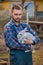 Farmer handsome European Caucasian rural portrait in the countryside with a beard, shirt and overalls looks at a white rabbit in