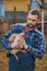 Farmer handsome serious european caucasian rural portrait in countryside with beard, shirt and overalls looks at chicken with