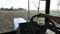 Farmer in hat, sits inside in the tractor cabin, rides on the field with plow.