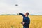 Farmer holds remote controller with his hands while quadcopter is flying on background. Drone hovers behind the