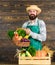 Farmer with homegrown vegetables. Fresh organic vegetables in wicker basket and wooden box. Man cheerful bearded farmer