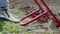 A farmer in jeans digs the ground with a red fork-shaped shovel. A miracle shovel, a handy tool