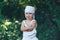 Farmer kid with yellow squash in white casual clothes overalls and hat, standing in garden and smiling, harvest time