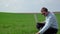 Farmer with laptop inspects wheat growth. Fresh green wheat field