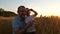 The farmer man and his son are satisfied with the wheat harvest, being on the field in the background of sunset. The