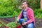 Farmer man transplanting tomato seedlings into open ground against green garden and country house. Spring work in kitchen-garden,