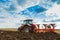 Farmer plowing stubble field with red tractor.