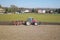 A farmer on a red tractor with a seeder sows grain in plowed land in a private field in the village area. Mechanization of spring