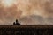 Farmer silhouette fighting fire in agricultural farming field with wall of smoke