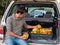 Farmer sits on the trunk of a car with crop of autumn pumpkin