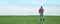 Farmer standing in wheat seedling field and using mobile phone app, smart farming concept, panoramic image