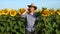 The farmer stands in field with sunflowers and talking on a cell phone.