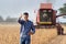 Farmer with tablet in front of combine harvester in soybean field