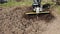 The farmer tills the soil using a rototiller, slow motion closeup.