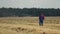 Farmer walks through farmland against the background of dusty combine harvesters