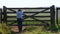 farmer walks to the wooden gate of a farm and observes the cassava plantation