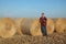 Farmer in wheat field after harvest with rolled straw in bale