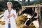 farmer in white robe posing background of cows in stall with milk