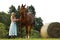 Farmer woman in dress stay beside chestnut horse near hay bale