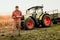 farmer working on field using smartphone in modern agriculture - tractor background