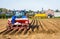 Farmers are planting a potato field using a tractor and a planter trailer in the belgian countryside