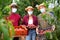 Farmers in protective mask posing with harvest of ripe peaches in orchard