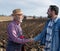 Farmers shaking hands in front of tractors in field