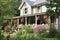 farmhouse with wrap-around porch, surrounded by flowers and greenery