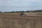 Farming tractor harrowing a dry field, after a summer harvest, and throwing up a lot of dust from the dry farmland