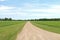 A farmland grass lined dirt road leading through agricultural fields with bright blue overcast sky perfect for seasonal marketing