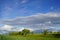 Farmland to the horizon. In the middle a row of fruit trees and above them gigantic clouds in the blue sky