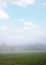 Farmstead in foggy landscape, grazing horse on the meadow, light blue sky with clouds