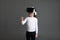 Fascinated female child in white long sleeve shirt looking into virtual reality glasses over grey background