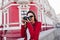 Fascinating female photographer working in morning in city. Outdoor photo of pleased young woman in red jacket and white