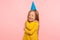 Fascinating lovely cute little girl with funny party cone on head embracing herself and keeping eyes closed