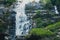 Fascinating low angle shot of a male admiring the waterfall in Doi Inthanon park in Thailand