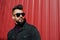 Fashion Arab man wear on black jeans jacket and sunglasses posed against red steel wall background. Stylish and fashionable