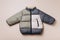 Fashion baby colorblock puffer jacket on grey background. Top view, flat lay. Newborn beige clothes outfit. Winter