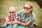 Fashion baby in sunglasses sitting with mother under the tree