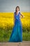 Fashion beautiful young woman in blue dress posing outdoor with cloudy dramatic sky in background. Attractive long hair brunette