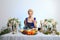 Fashion blonde model with colorful makeup sitting behind festive decorated table and eating felt shoe