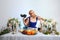 Fashion blonde model with colorful makeup sitting behind festive decorated table and eating felt shoe